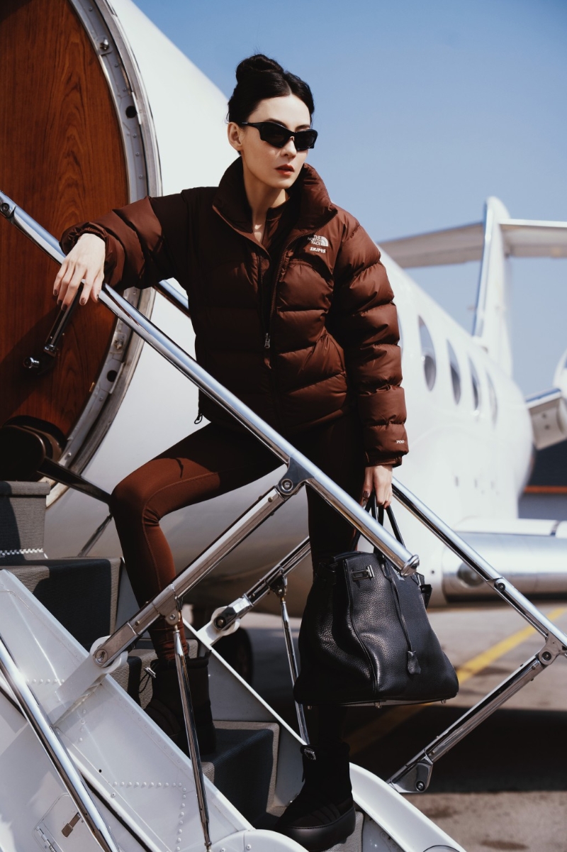 扎起丸子頭的張栢芝身穿一件棕色羽絨服及同色貼身連體衣，再配上黑色短靴及墨鏡，完美地襯托出她的纖幼身形，整體造型既保暖又充滿時尚氣息。