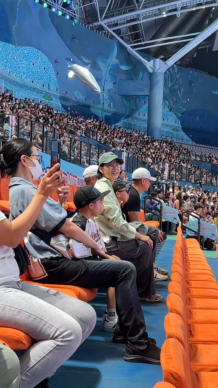 胡杏兒頭戴綠色Cap帽及身穿淺綠色襯衫，與家人一起坐在VIP區域觀看演出，她臉上掛滿笑容，時不時還揮手互動，看起來心情大好。