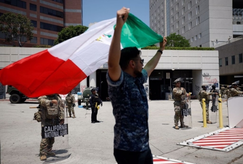 1名男子10 日高舉墨西哥國旗，在洛杉磯市中心的加州國民警衛隊成員面前抗議。路透社